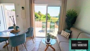 Una sala de estar con un sofá, una mesa de comedor con sillas, una pequeña mesa de centro y vistas al exterior a través de un ventanal corredera.