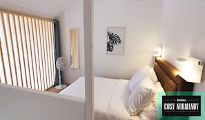 Un dormitorio con cama, mesita de noche, ventilador de pared y una obra de arte con hojas enmarcada.