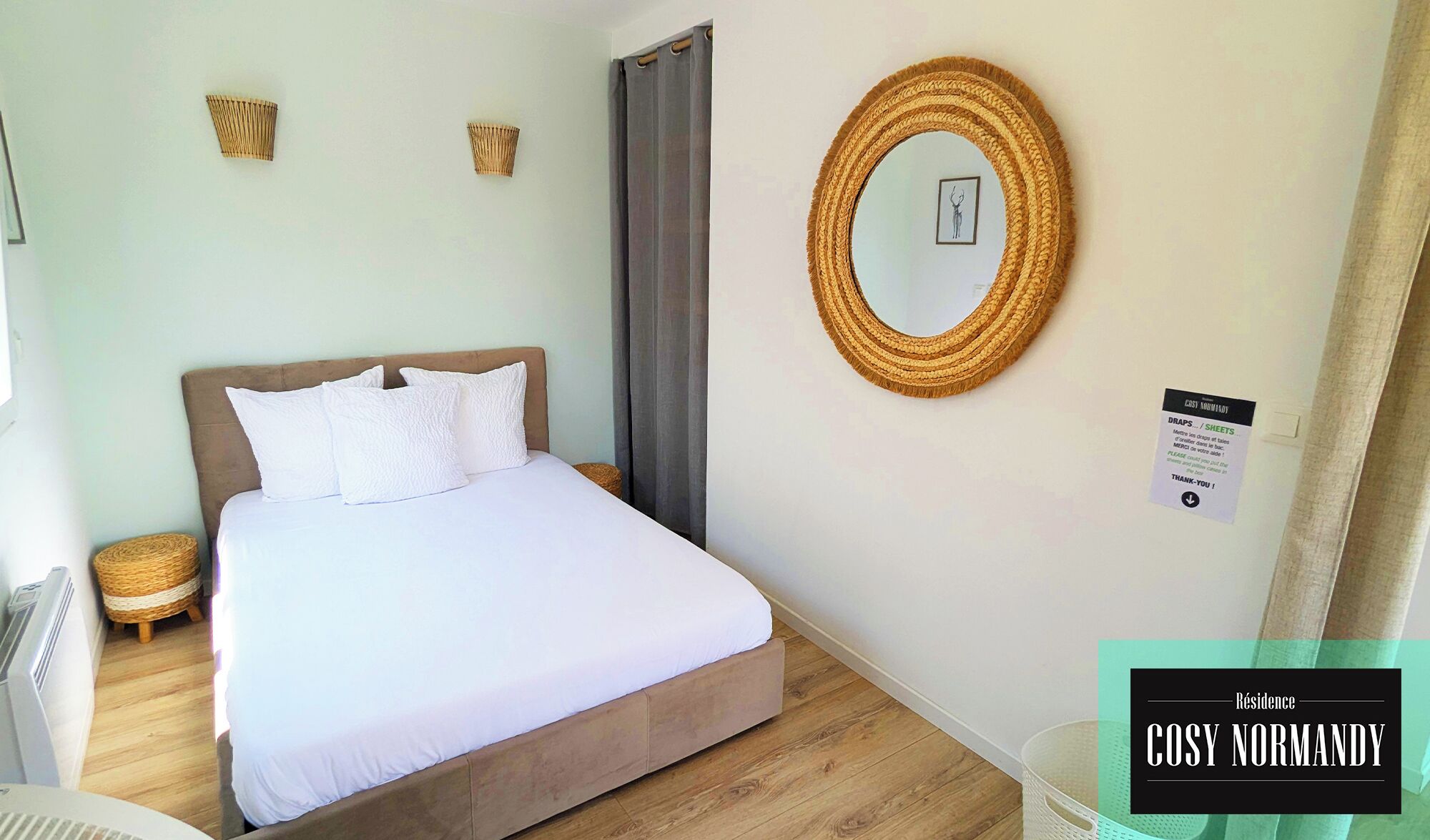 Une chambre à coucher avec un lit, deux paniers fixés au mur, un miroir rond et un panneau avec du texte.