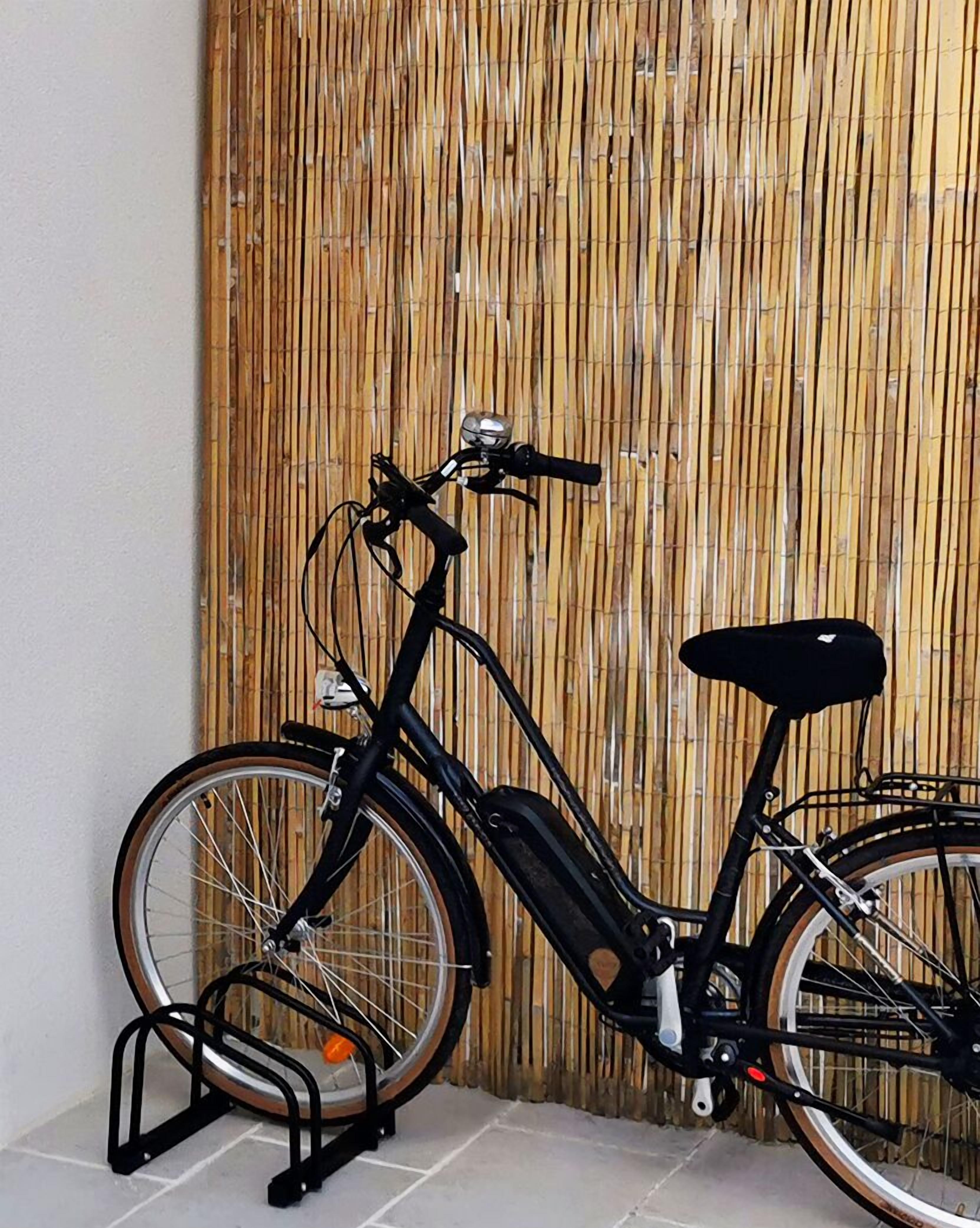 Ein stehendes Fahrrad mit Korb und Stütze, an eine Bambuswand gelehnt.
