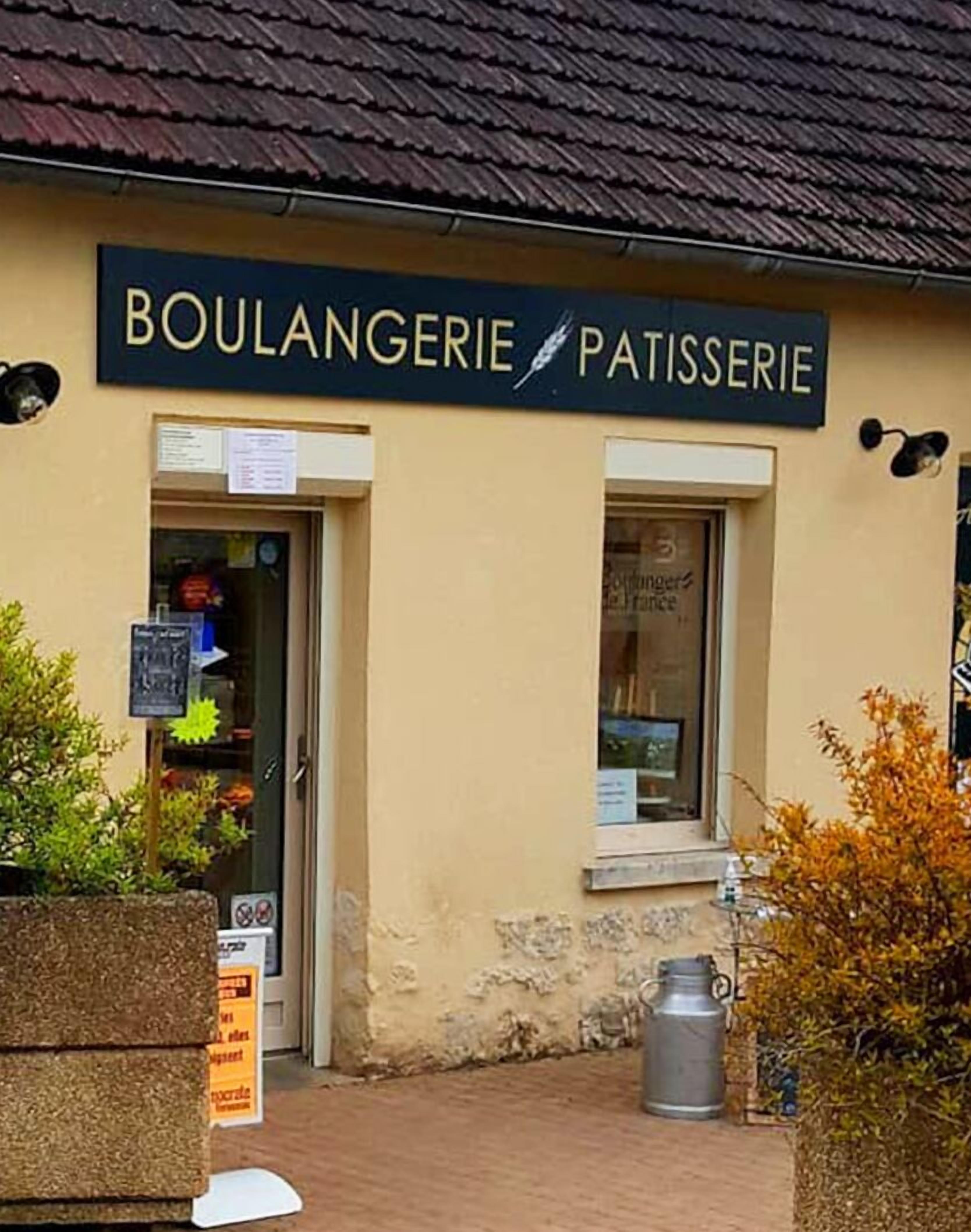 Een bakkerij/patisserie met een bord boven de ingang, een raam met een menukaart en een metalen prullenbak buiten.