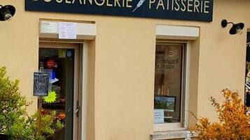 Een bakkerij/patisserie met een bord boven de ingang, een raam met een menukaart en een metalen prullenbak buiten.