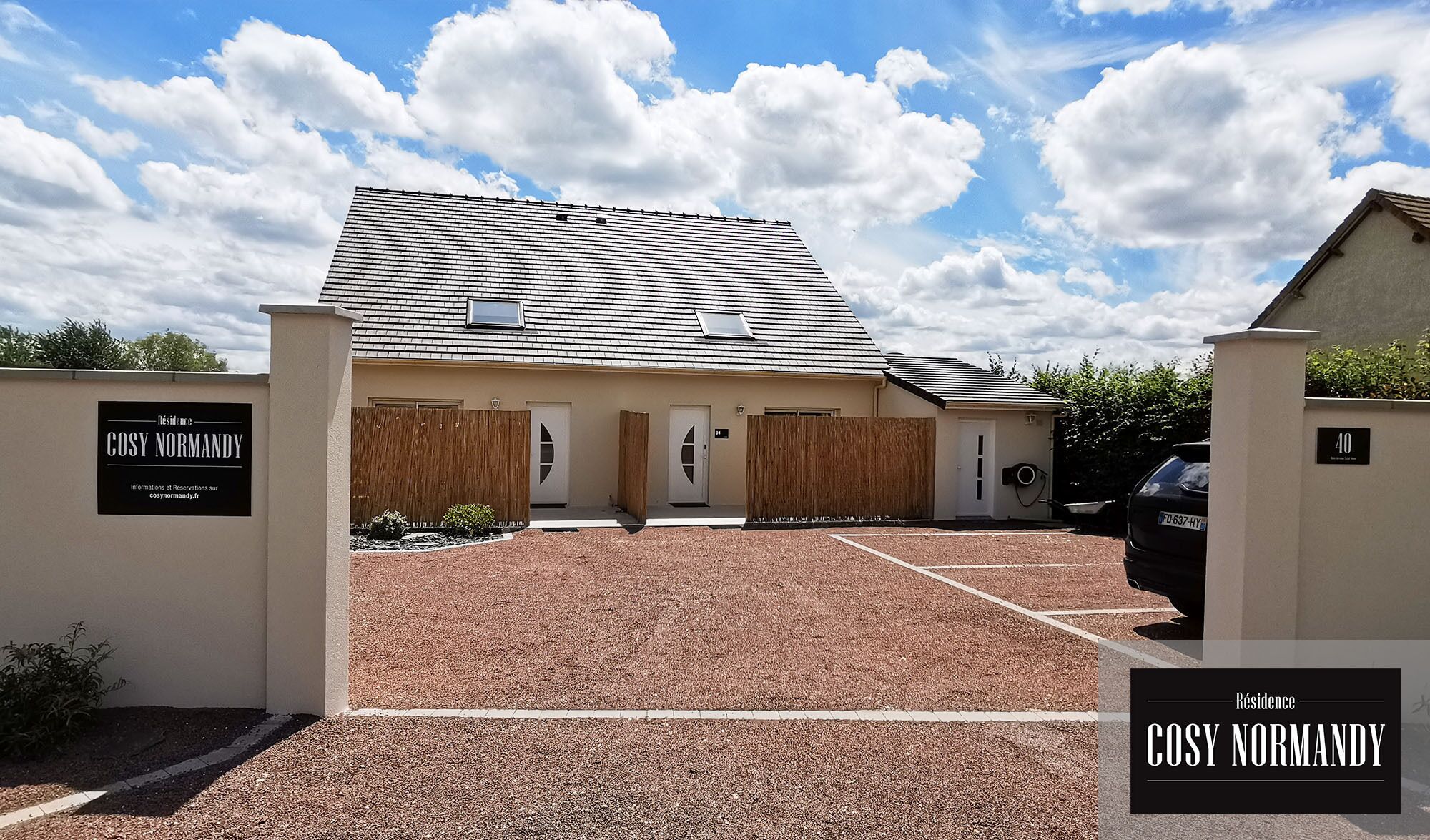 A residential property named 'Cosy Normandy' with a gravel driveway, wooden fencing, and a car parked in the driveway.