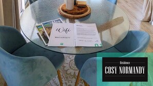 Una sala moderna con una mesa redonda de vidrio, sillas azules, una lámpara colgante y un sofá con cojines estampados.