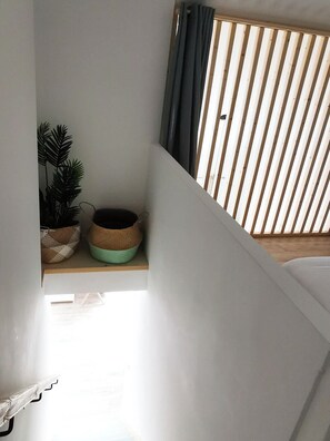 Una escalera con barandilla de madera, una planta en maceta y un estante con adornos.