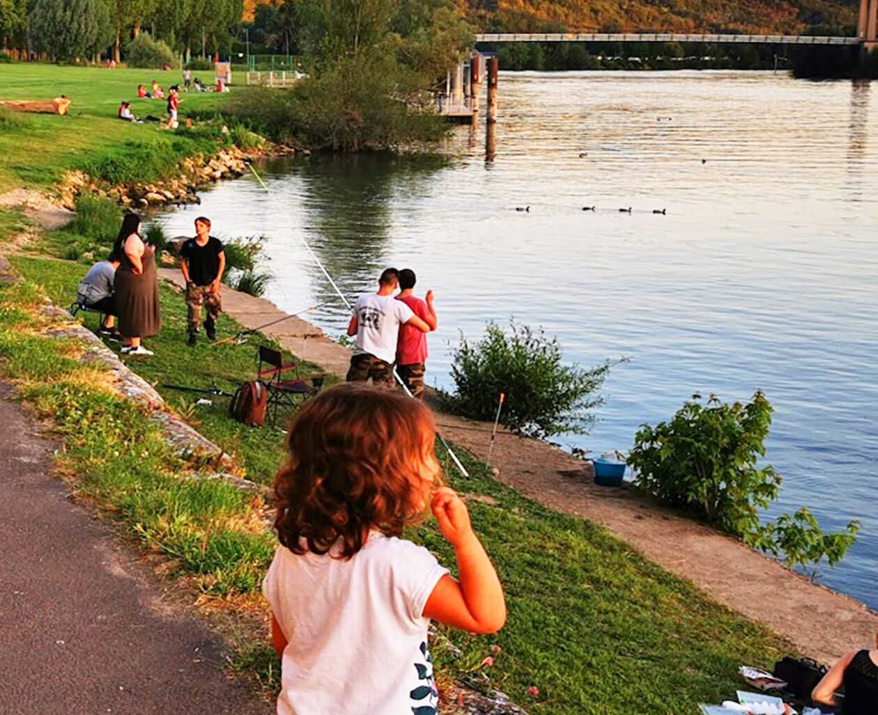 Un parco lungo il fiume, con persone che passeggiano e si siedono sull'erba.