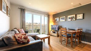 A modern living room with a sofa, a dining table with chairs, a TV, and a balcony with a view. - Modern, Spacious City Apartment, Lift, Balcony, Free Wi-fi & Parking, Fab views, (Edinburgh)