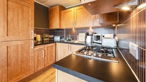 A modern kitchen with wooden cabinets, a gas stove, a microwave, and a coffee maker. - Modern, Spacious City Apartment, Lift, Balcony, Free Wi-fi & Parking, Fab views, (Edinburgh)