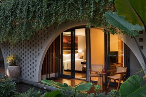 A modern hotel room with a large sliding glass door leading to a balcony, a seating area with a table and chairs, and a potted plant. - Beachwalk Residence (Kuta)
