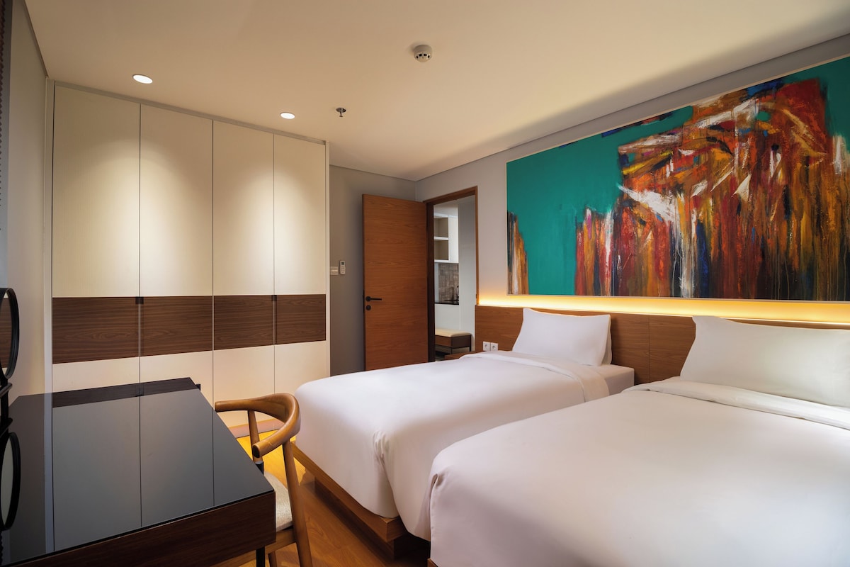 A hotel room with two beds, a desk, and a large abstract painting on the wall.