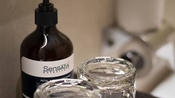 Una botella de jabón de manos Sensatia Botanicals junto a dos recipientes de vidrio transparente.