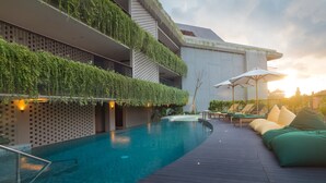 Zona de piscina con terraza de madera, sillas de descanso y un edificio con jardines verticales.