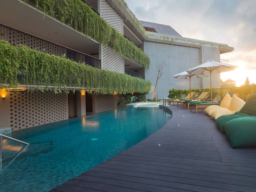 Zona de piscina con terraza de madera, sillas de descanso y un edificio con jardines verticales.