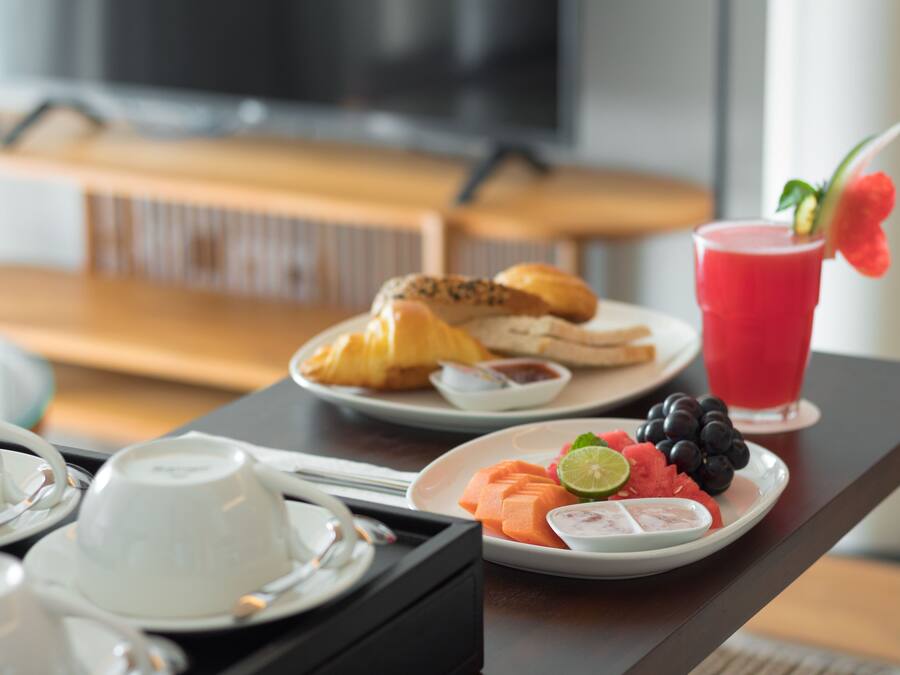 Een ontbijtkarretje met croissants, een fruitschaal met watermeloen, druiven en een limoen, en een rood drankje met garnering.