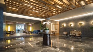 Un vestíbulo amplio con suelo de mármol pulido, paneles de techo de madera e iluminación moderna.