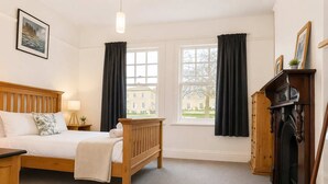 Ein Hotelzimmer mit einem hölzernen Bett, einem Nachttisch, einer Lampe, einem Kamin und Blick auf ein Gebäude durch die Fenster.