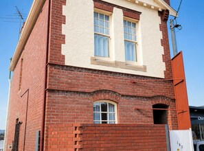 Um edifício de tijolos vermelhos com duas janelas e uma pequena janela arqueada abaixo.