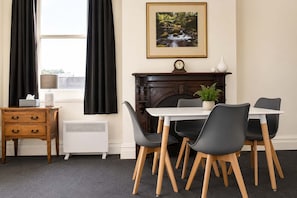 A room with a dining table, chairs, a fireplace, a clock, and a radiator.