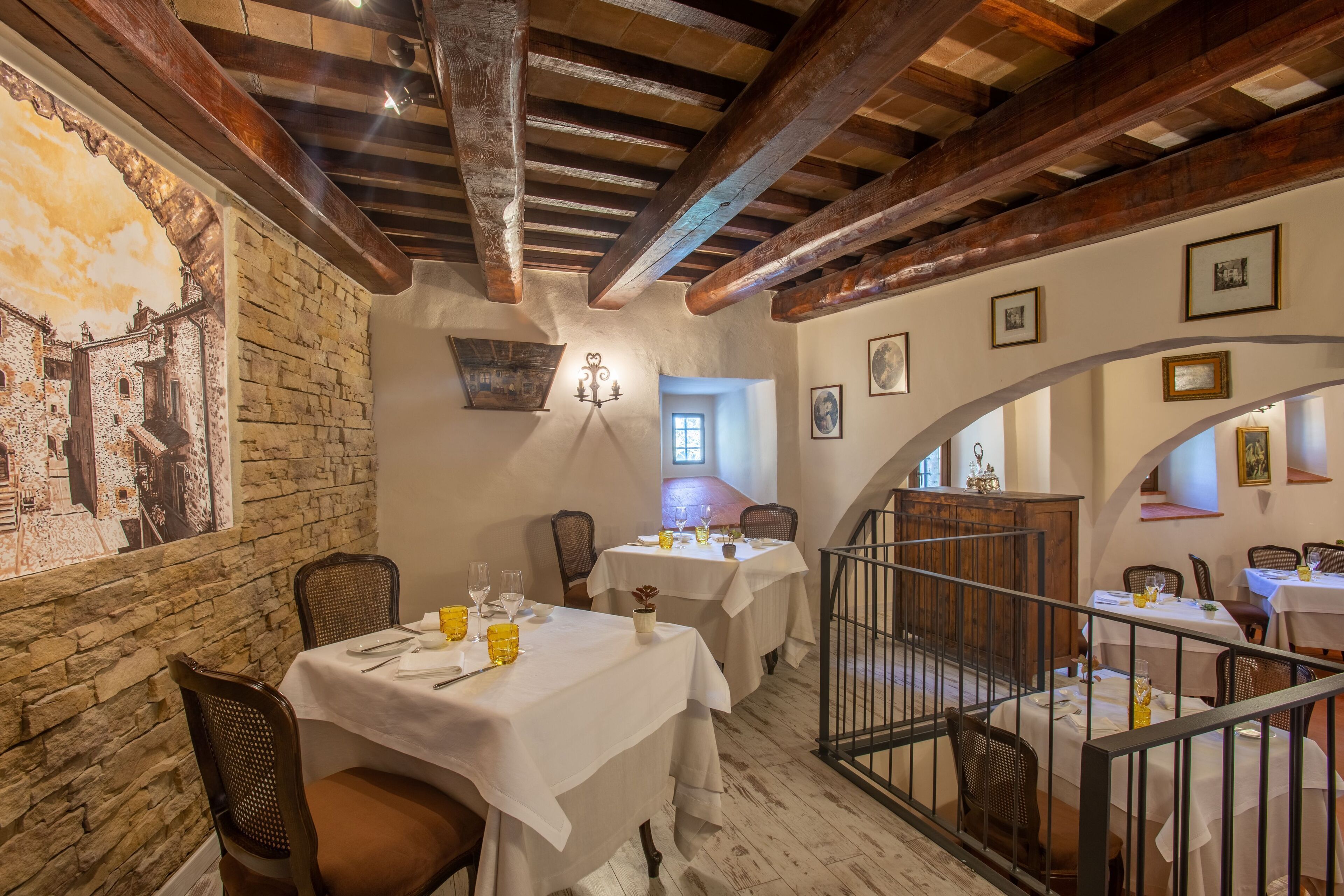 Un comedor con paredes de piedra, vigas de madera y manteles blancos. Las mesas están dispuestas con sillas, vasos y cubiertos.