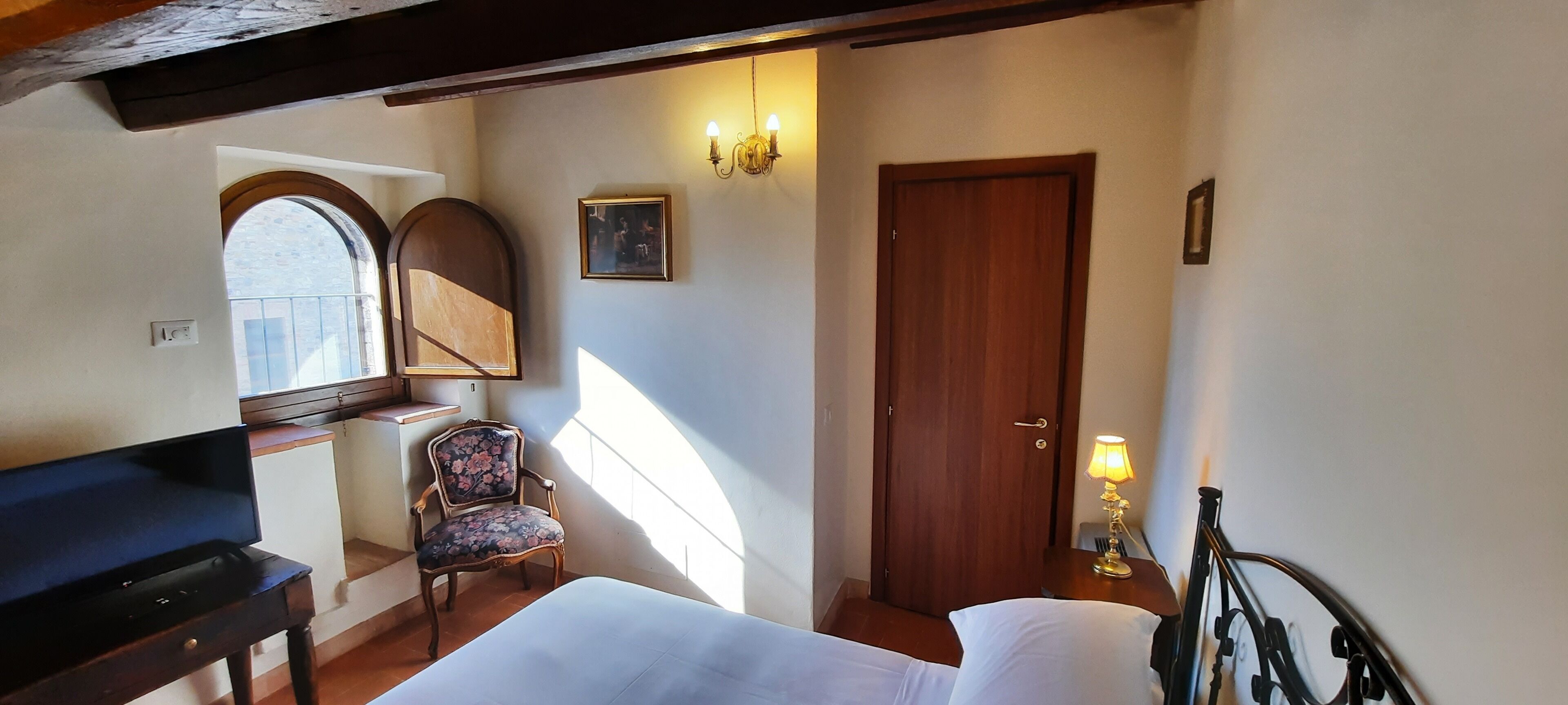 Ein Schlafzimmer mit einem Bett, einem Sessel, einem Fernseher, einer Tür und einem Fenster.