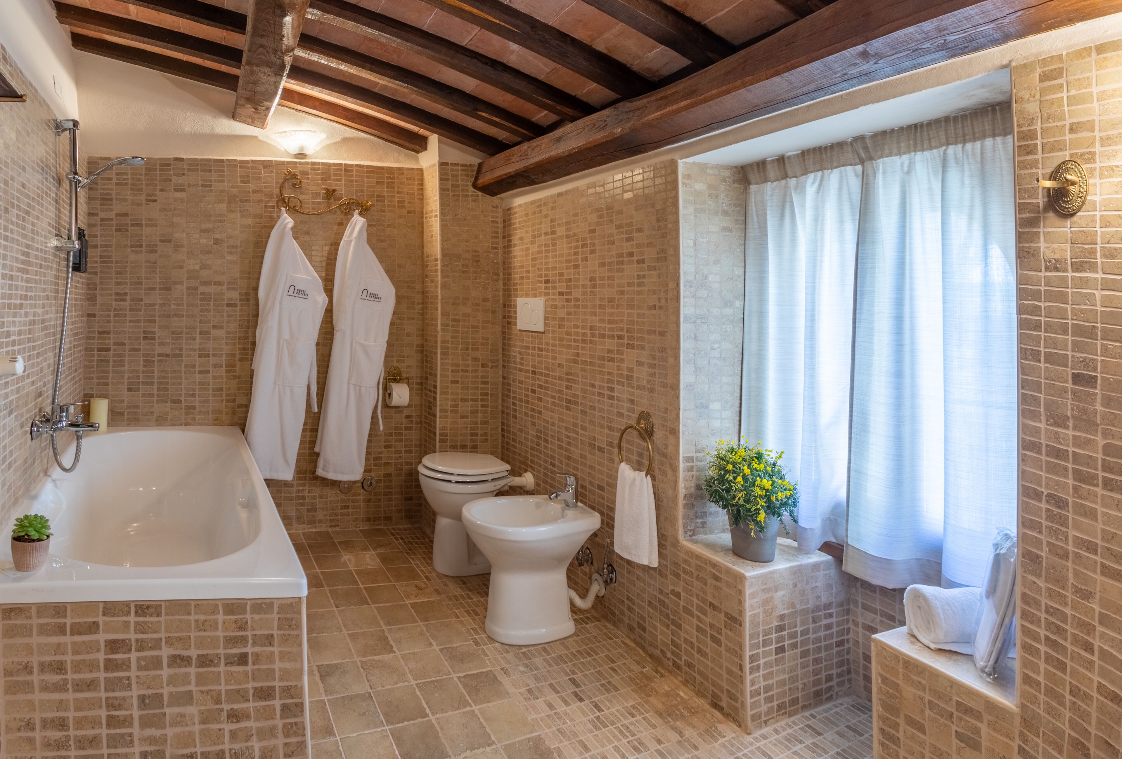 Un baño con bañera, inodoro, bidé y una ventana con cortinas.