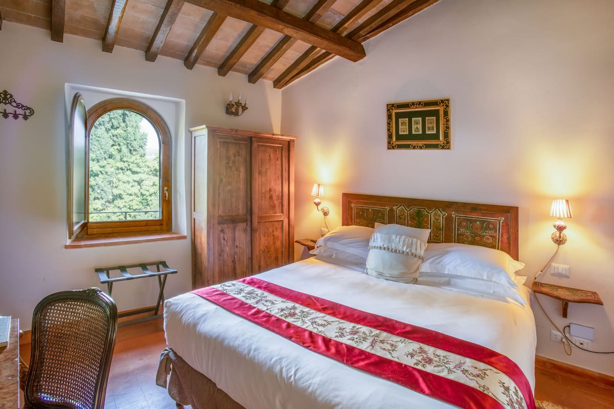 Un dormitorio con una cama grande, vigas de madera en el techo, una ventana con vistas a árboles y un armario de madera.