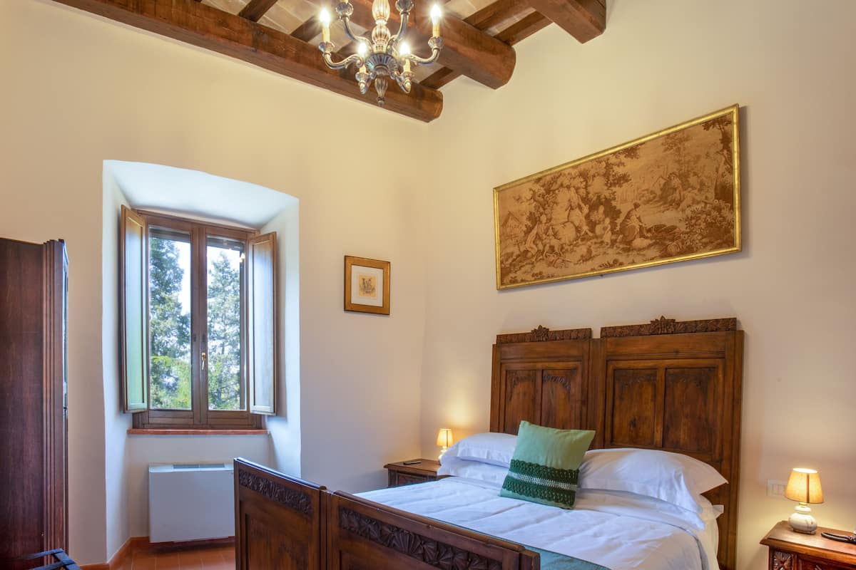 Un dormitorio con techo de madera, un candelabro, una cama con almohada verde, un cuadro grande enmarcado y una ventana.