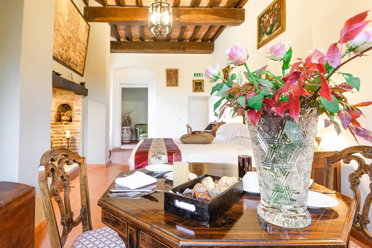 Un comedor con una mesa de madera, sillas, un florero con flores y una chimenea de ladrillo.