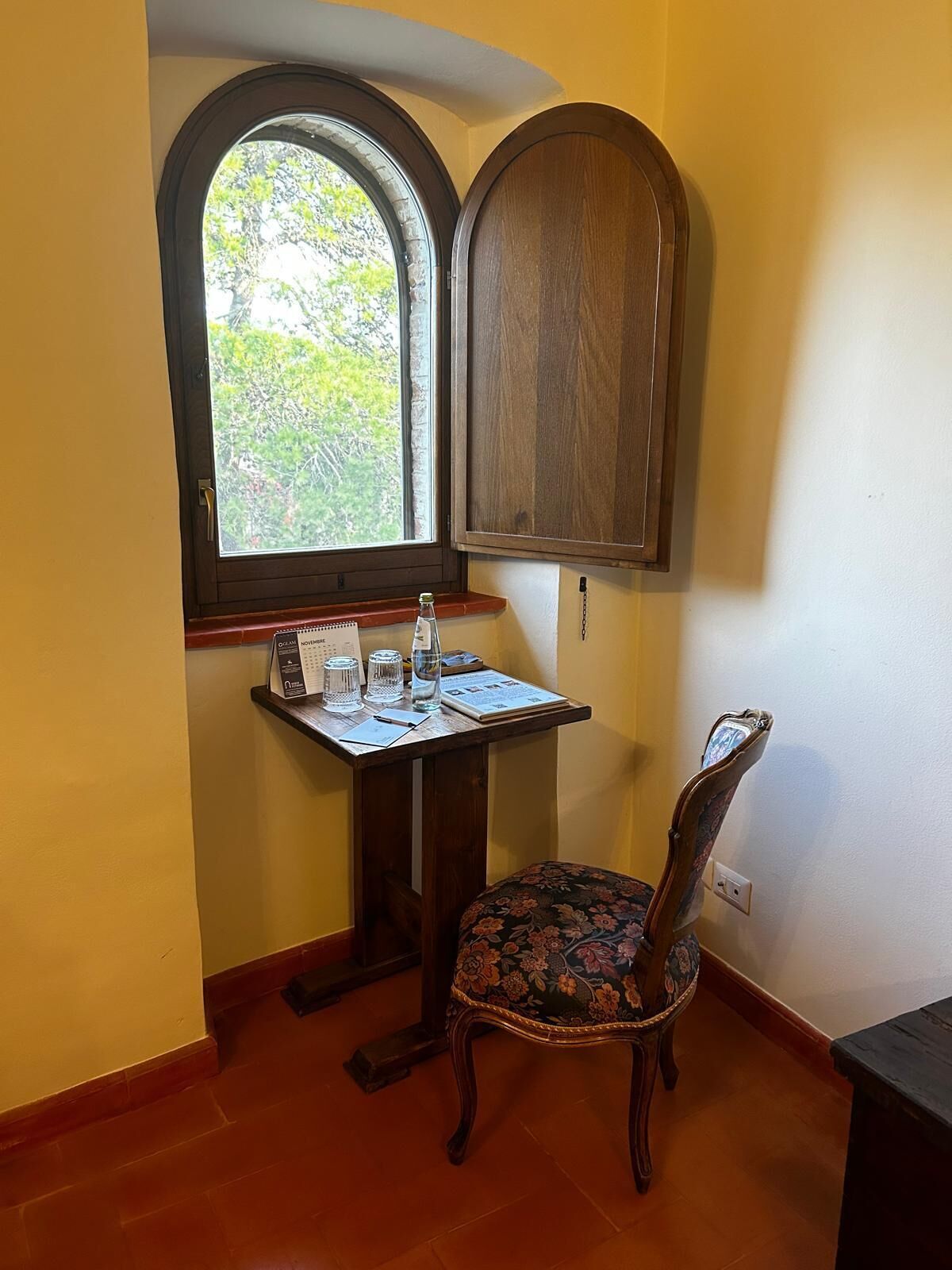 Una habitación de esquina con un mueble de madera, una mesita con un cuaderno, gafas y una botella de agua.