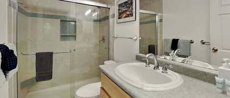 A bathroom with a glass-enclosed shower, a toilet, a sink with a mirror, and a towel rack.