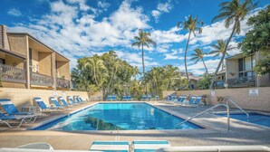 Une piscine bordée de chaises longues bleues, de palmiers et surplombée d’un ciel dégagé.