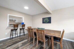 A dining area with a wooden table and four chairs, a kitchen with a stainless steel range hood, and a wall-mounted sign. - Walk-In 3BR | Arcade + Indoor Pool | Pointe Royale (Branson)