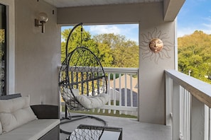 Relax on the balcony with a comfortable sofa, wicker chair, and hanging chair, taking in the serene views of the lush green landscape.