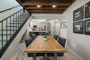 Enjoy meals in this stylish dining area with a long table and black leather chairs, surrounded by framed photographs and a potted plant.