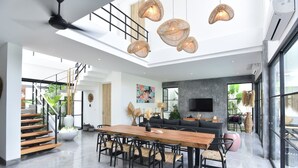 A spacious living area with a high ceiling, a wooden dining table, black chairs, and woven pendant lights. - Villa Soho (Canggu)