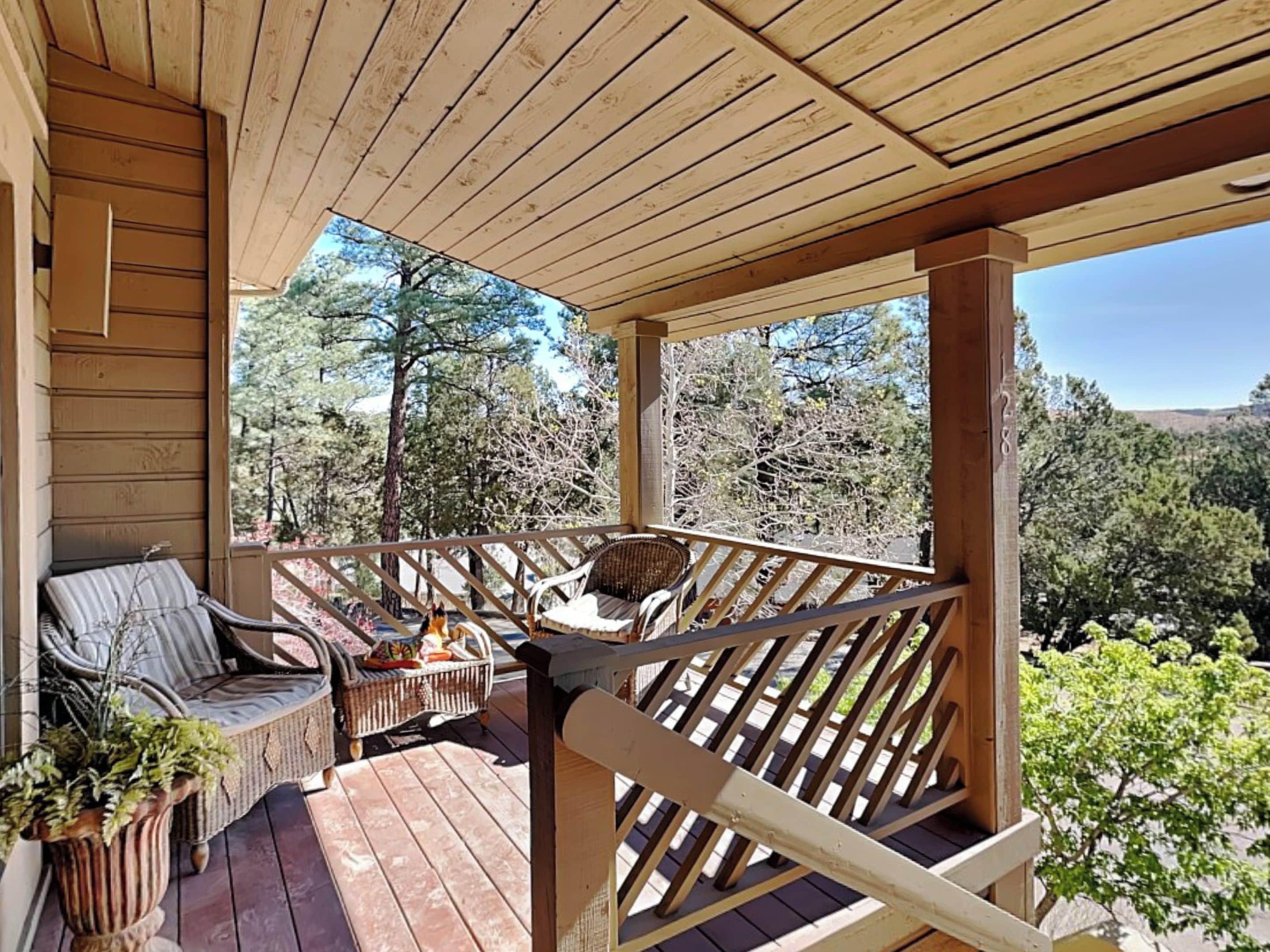 A wooden deck with a railing, a wicker sofa, and a potted plant.