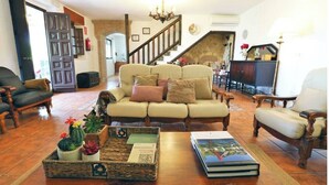 Ein gemütliches Wohnzimmer mit einer Couch, Sesseln, einem Couchtisch mit Büchern und Pflanzen, einer Treppe und einem Kamin.