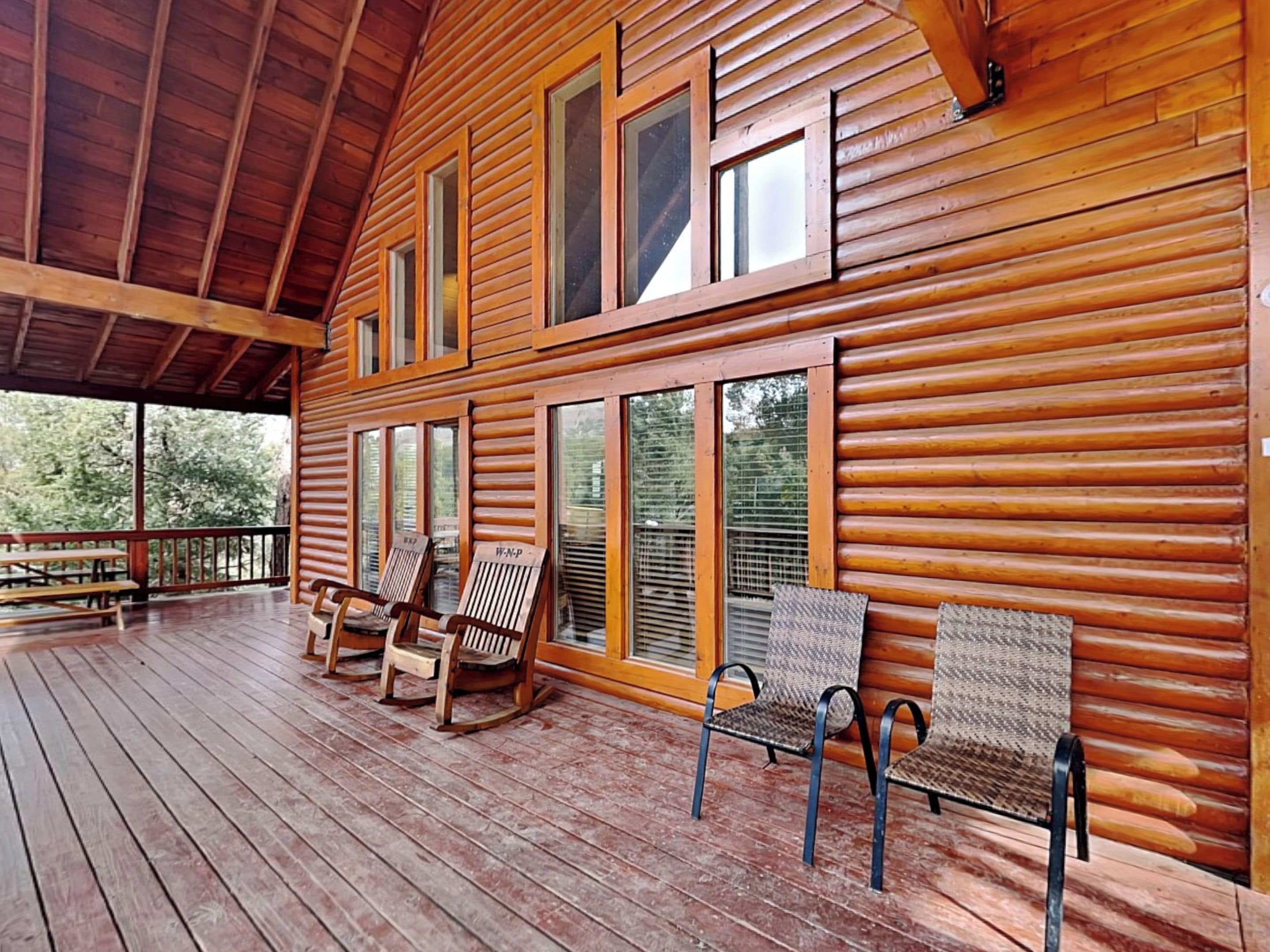 A wooden cabin with a covered porch, rocking chairs, and a bench.
