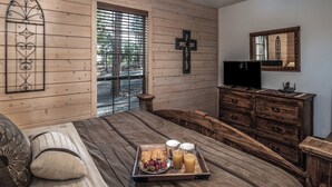 A bedroom with a wooden bed, a wooden dresser, a television, and a cross on the wall. - Wine N Pines by Ruidoso Vacation Rentals (Alto)