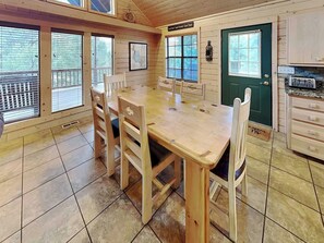 Una mesa de comedor de madera con sillas, una puerta verde y una zona de cocina con armarios.