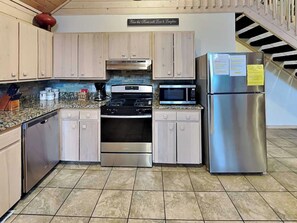 Una cocina con armarios de color claro, un refrigerador de acero inoxidable, un microondas, una estufa y un lavavajillas.
