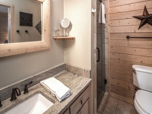 A bathroom with a granite countertop, a sink, a mirror, a towel, a shower, and a toilet. - Wine N Pines by Ruidoso Vacation Rentals (Alto)