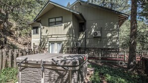 A two-story house with a stone exterior, a covered patio, and a fenced yard. - Tis Holiday Haus by Ruidoso Vacation Rentals (Ruidoso)