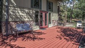 A wooden deck with a red floor, a stone wall, and a bench with striped cushions. - Tis Holiday Haus by Ruidoso Vacation Rentals (Ruidoso)
