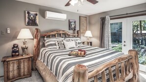 A bedroom with a wooden headboard, a bed with striped bedding, two bedside tables with lamps, and artwork on the walls. - Tis Holiday Haus by Ruidoso Vacation Rentals (Ruidoso)