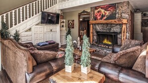 A spacious living room with a fireplace, leather sofas, a staircase, and a flat-screen TV. - Tis Holiday Haus by Ruidoso Vacation Rentals (Ruidoso)