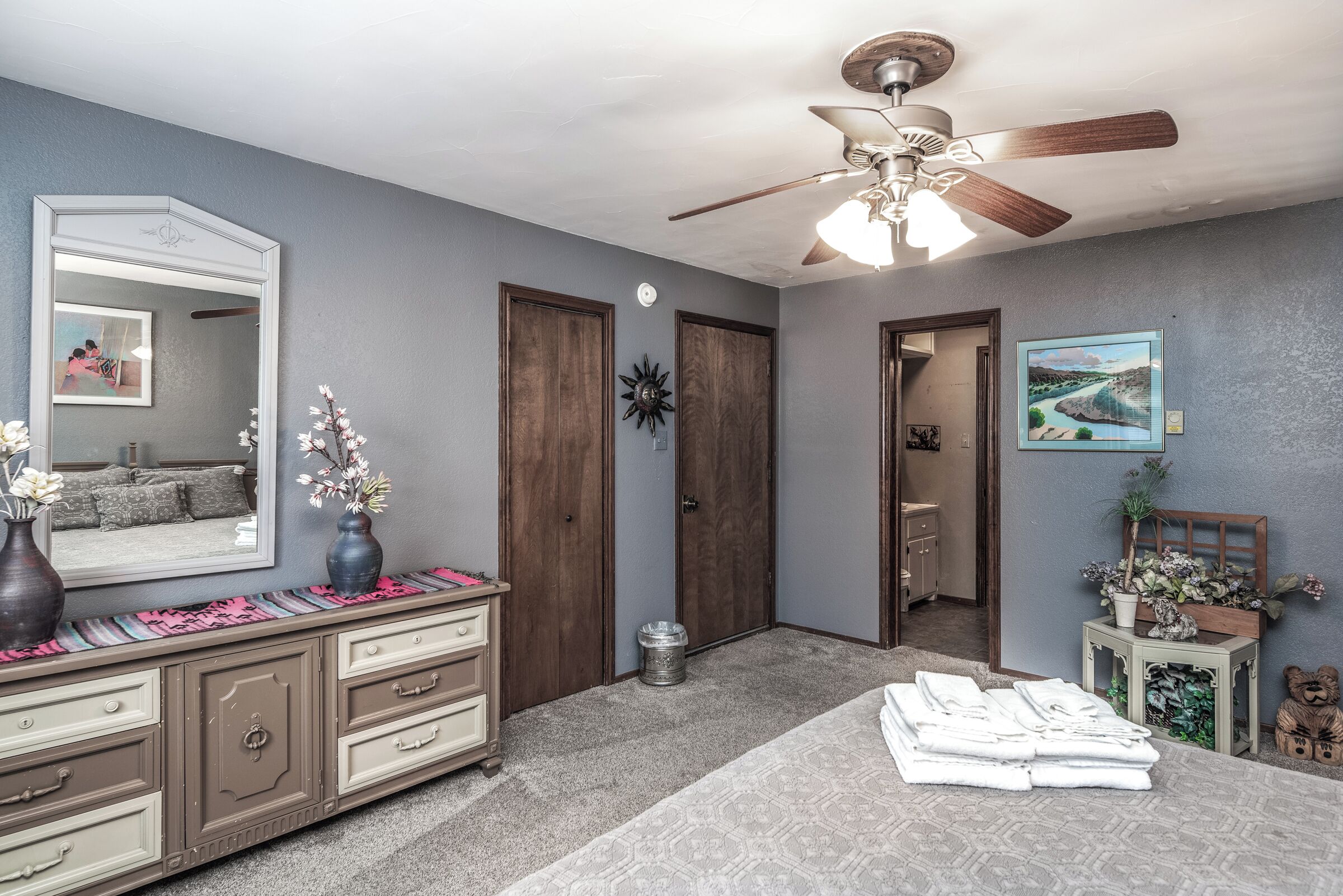 A bedroom with a bed, dresser, vanity, and a ceiling fan.