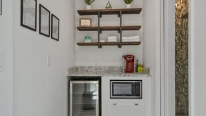 Una cocina con horno empotrado, cafetera y refrigerador pequeño. Hay repisas sobre la encimera con toallas y un certificado enmarcado.