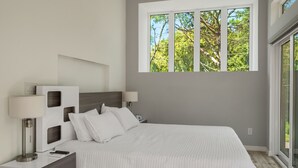 Un dormitorio moderno con una cama grande, dos mesitas de noche y una ventana con vistas a árboles.