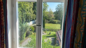 Une fenêtre donnant sur un jardin et un bâtiment dont le toit est recouvert de tuiles.
